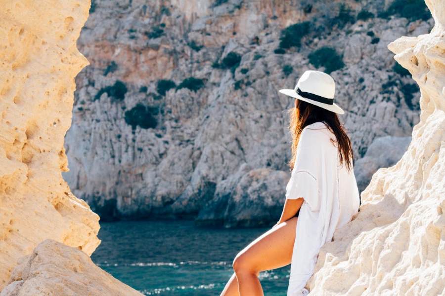 Single vrouw met zonnehoed en witte outfit op het strand